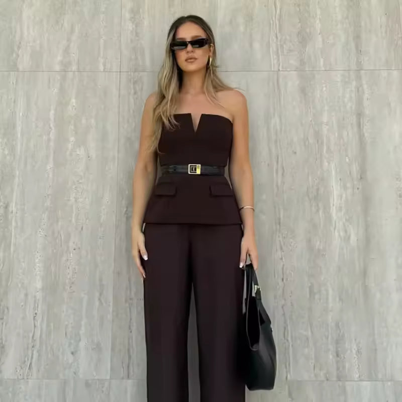 Woman in a brown strapless top and wide-leg pants standing against a light gray