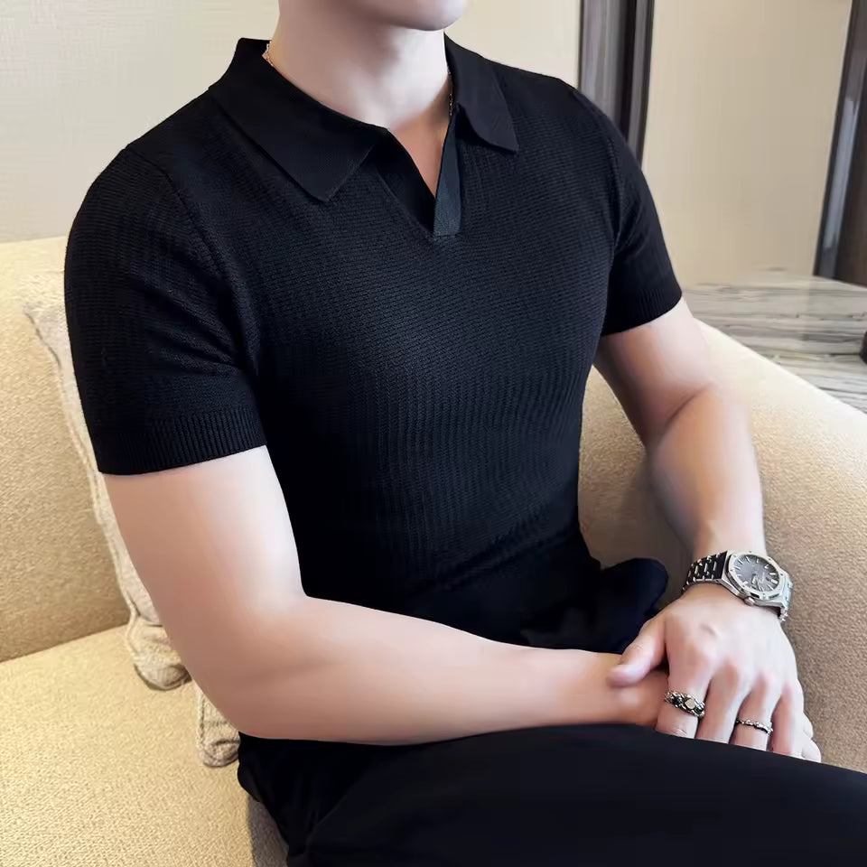 Person wearing a black short-sleeve polo shirt sitting on a beige couch.